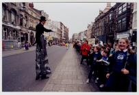 Man walks down street on stilts watched by...