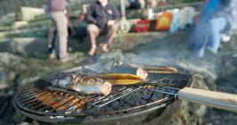 Close-up of BBQ with fish and a group of people...